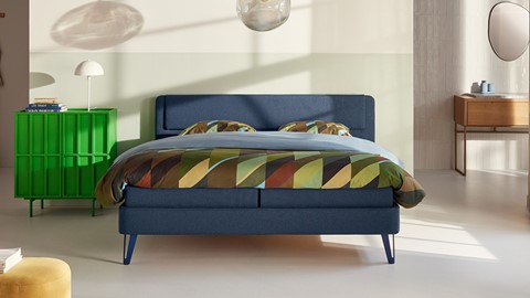 een bed met een blauw hoofdeinde en kleurrijk beddengoed