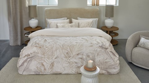 een bed met een wit beddengoed en een kaars op een tafel