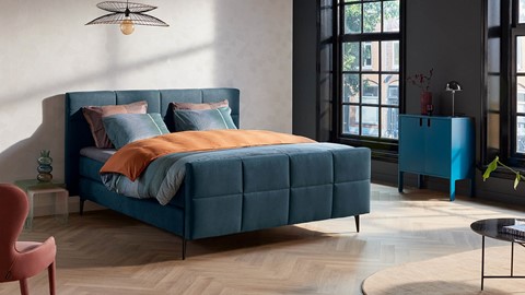 Een blauw bed met oranje kussens