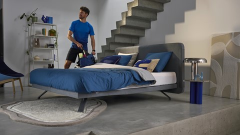 Een man die een tas naast een bed draagt