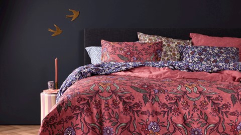 een bed met een roze bloemendekbed en kussens