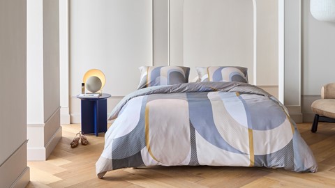 een bed met een kleurrijk dekbed en een lamp op een tafel