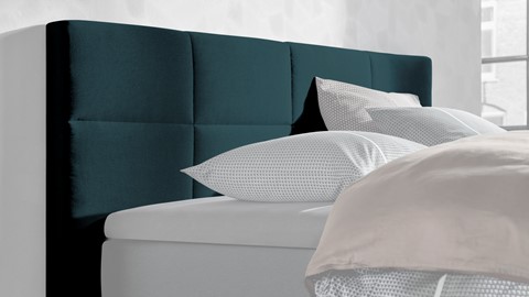 een bed met kussens en een blauw hoofdeinde