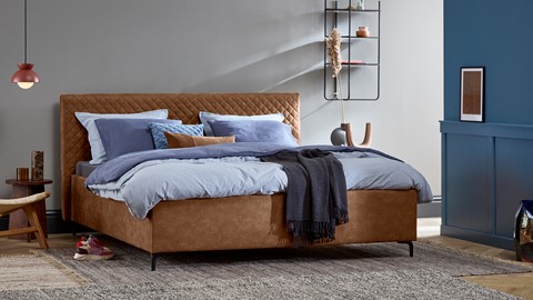 een bed met een bruin hoofdeinde en blauwe kussens