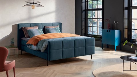 Een blauw bed met oranje kussens