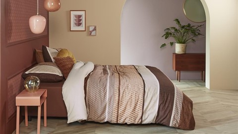 een bed met een bruin dekbed en een plant in een kamer