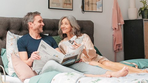 Een man en een vrouw die op een bed zitten en een krant lezen