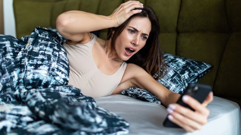 Een vrouw die in bed ligt en een telefoon bekijkt