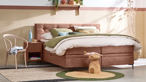 een bed met een roze hoofdeinde en groene kussens