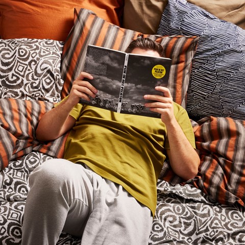 Man leest boek in bed op veel kussens
