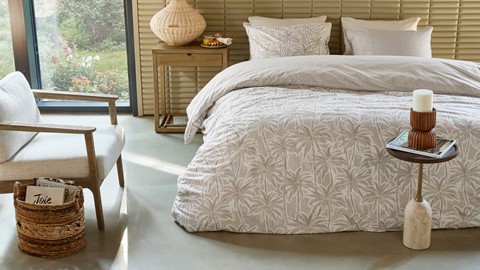 Een bed met kussens en een vaas op een tafel