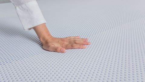 Hand duwt op een koudschuim matras van Maxi