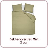 Een bed met kussens en een groene deken
