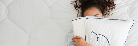 Een vrouw die op een bed ligt en een kussen vasthoudt