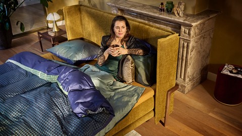 Een vrouw die op een bed zit en een kopje vasthoudt