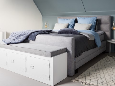 een bed met een bankje en een kleed