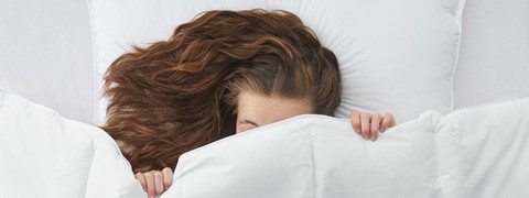 een vrouw die in bed ligt met haar hoofd bedekt met een wit kussen
